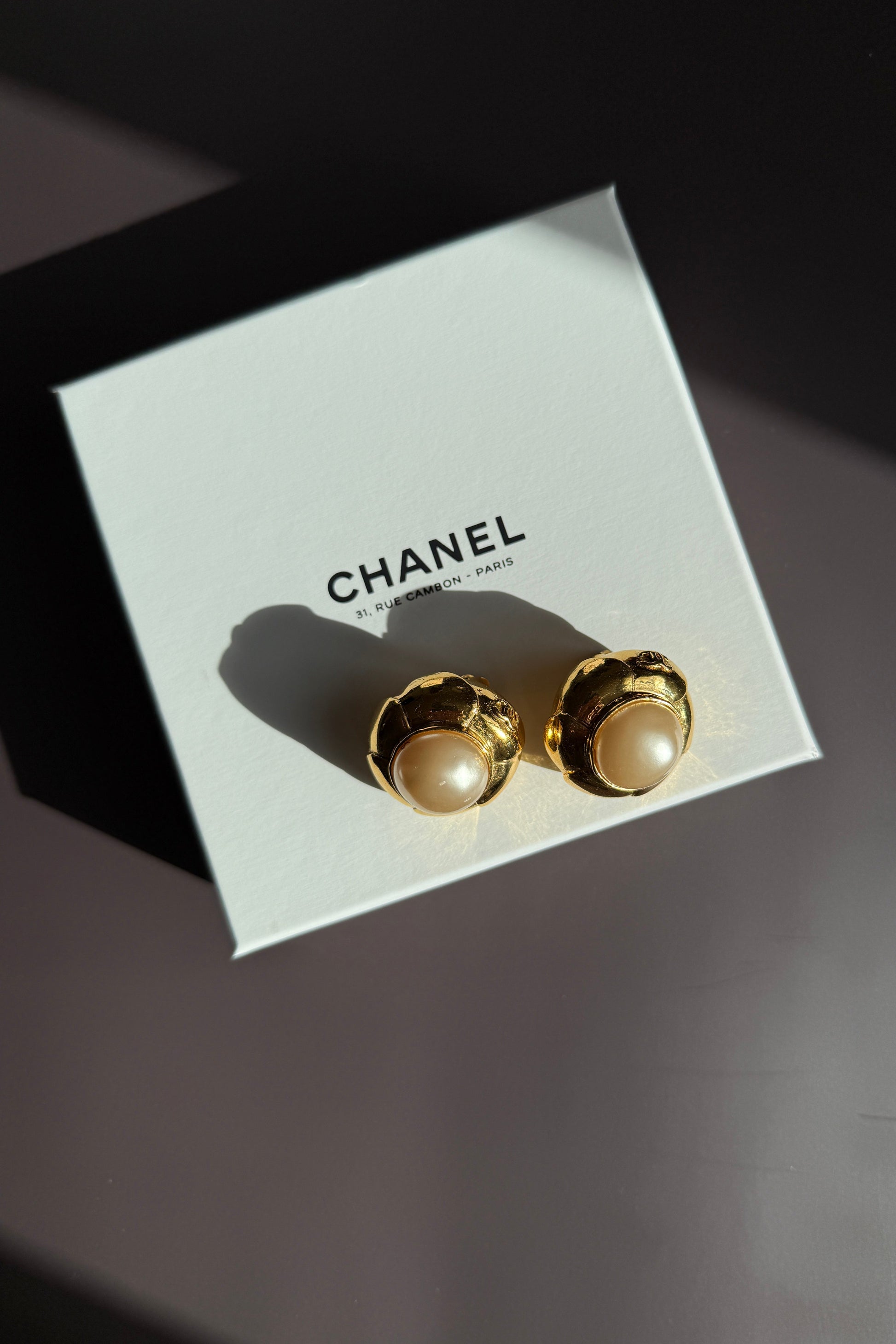 Clips d’oreilles Chanel vintage en métal doré avec perle baroque, présentés sur boîte Chanel blanche.