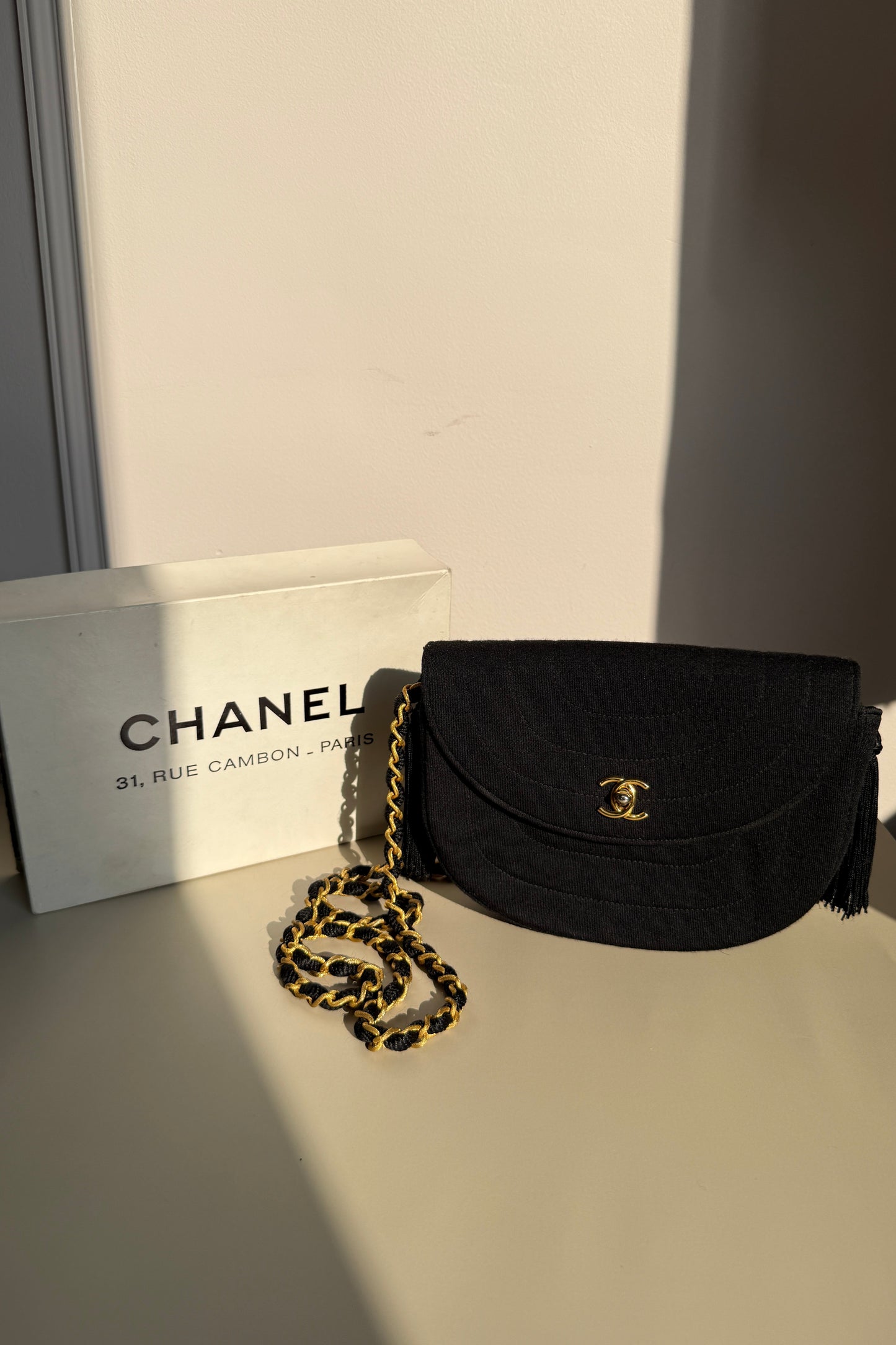 Sac Chanel vintage en tissu matelassé noir avec chaîne dorée, présentée avec sa boîte d’origine rue Cambon Paris.