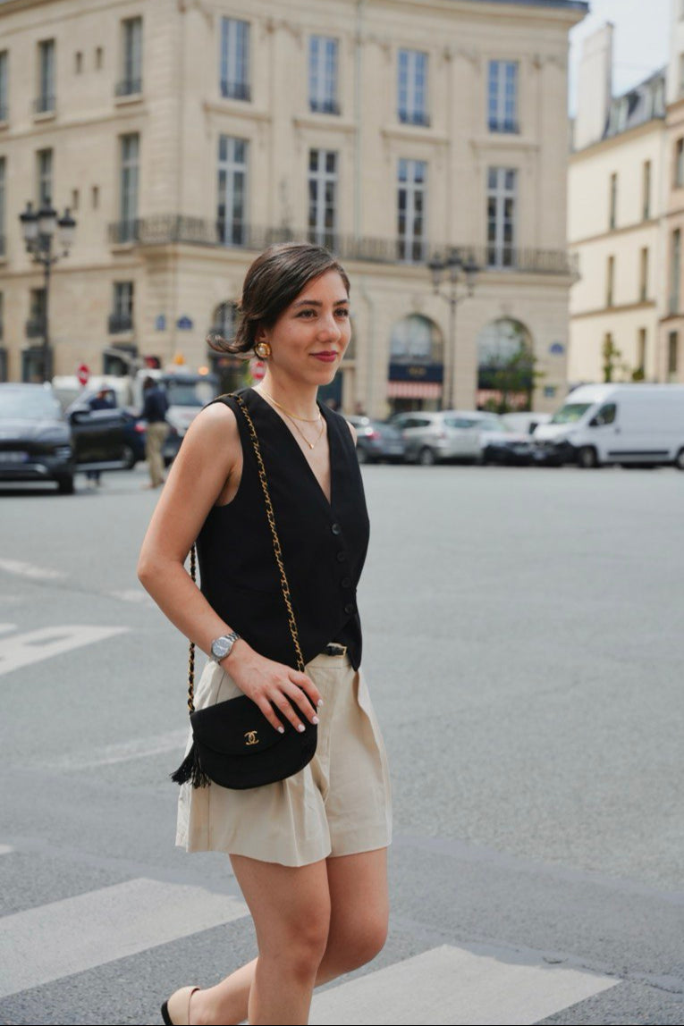 Woman walking on a street in an urban setting with buildings and cars in the background having a Chanel vintage bag on shoulder